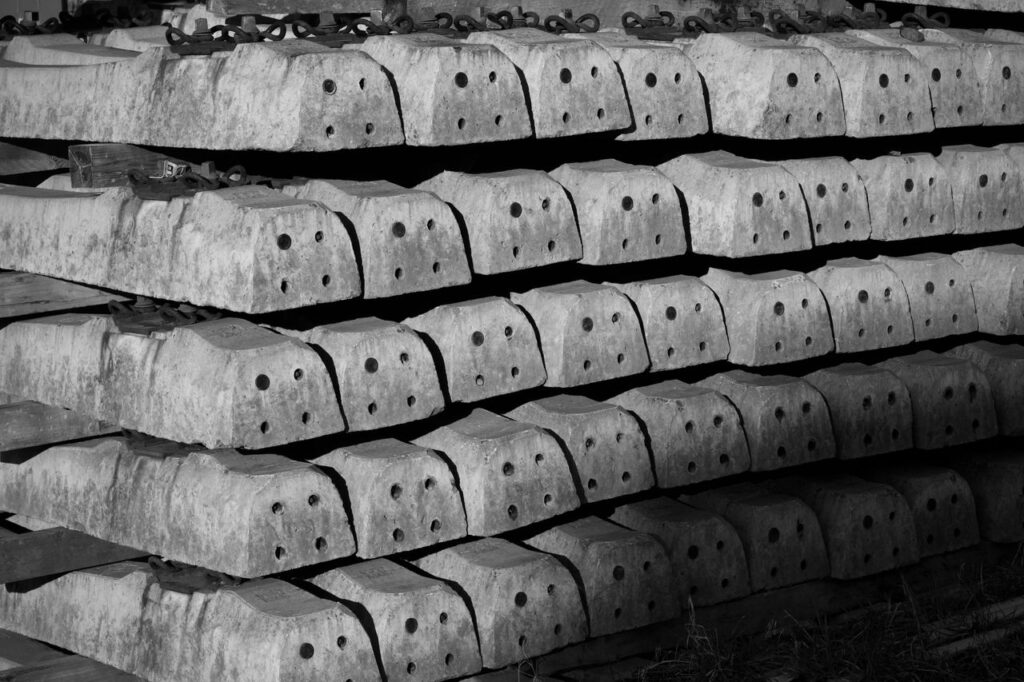 Monochrome photo of stacked concrete railroad sleepers with a distinct pattern.
